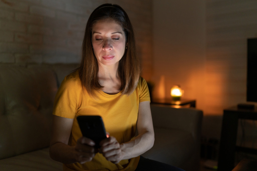 Woman checks her phone for alerts during a winter storm blackout at home.